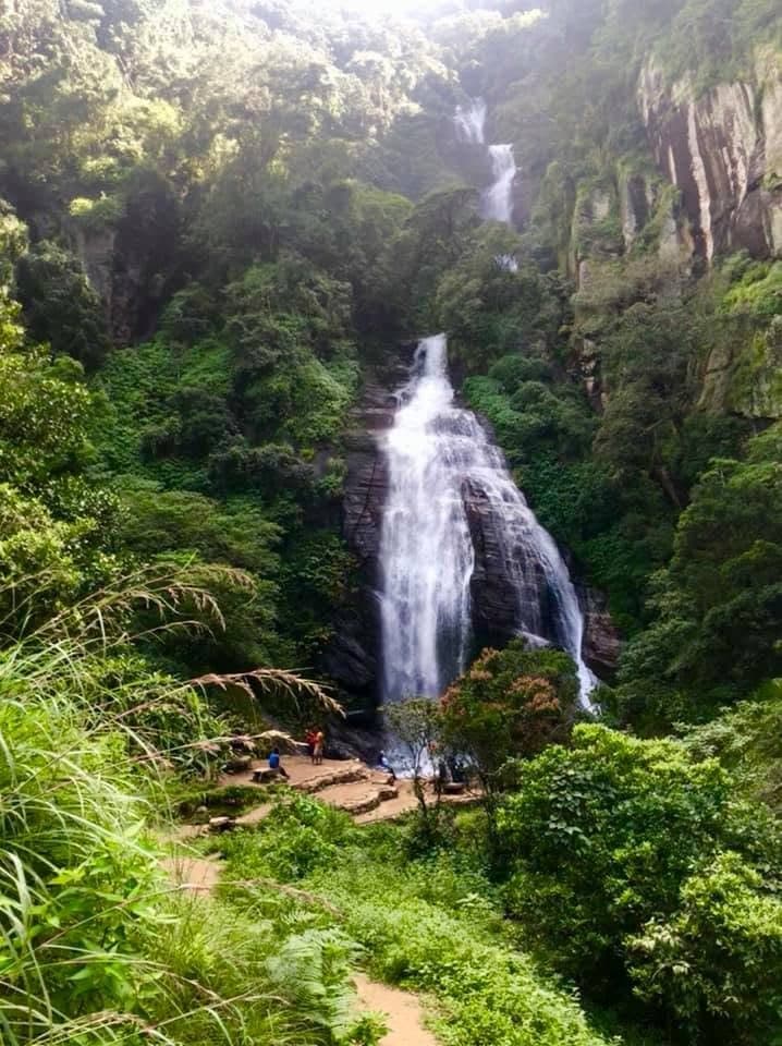 A tall waterfall cascading through dense forest in Sri Lanka's hill country