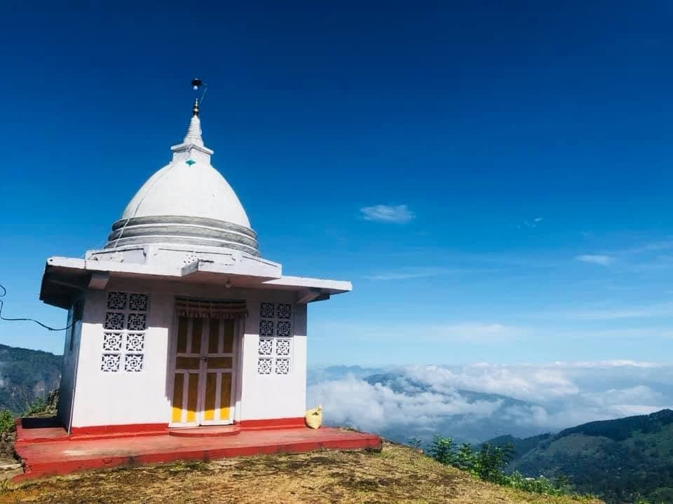 A small white shrine with a golden spire on a hilltop above the clouds