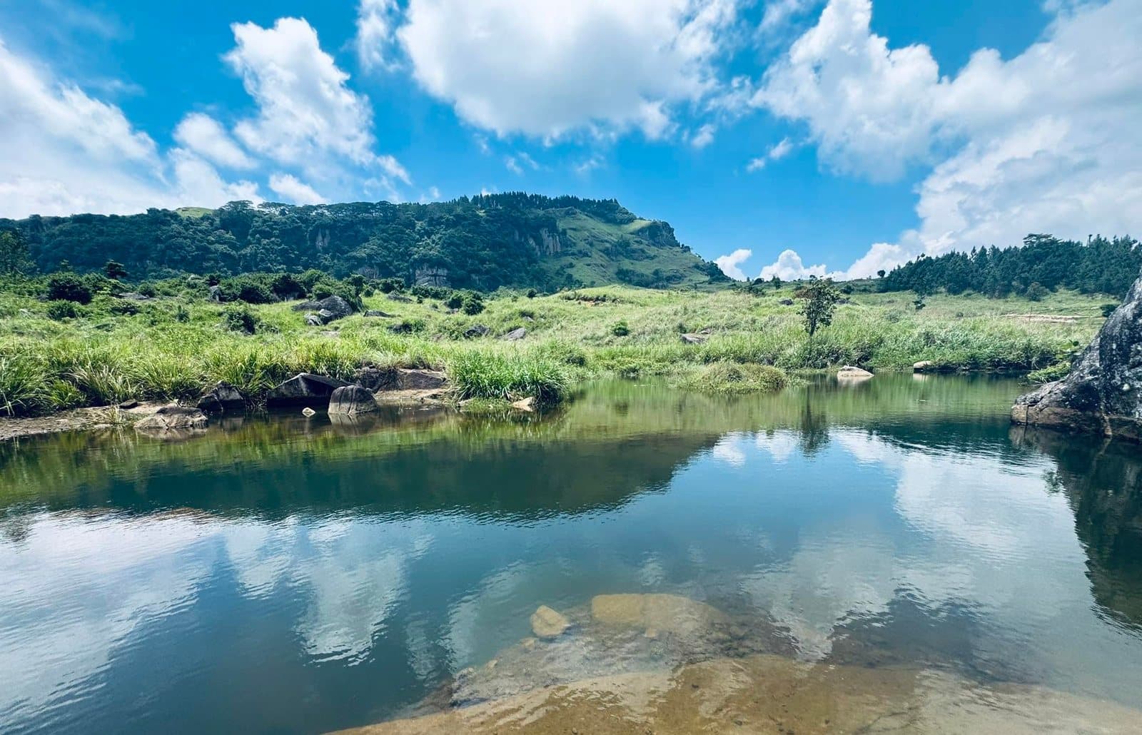 A clear mountain stream running through grassland with hills in the background