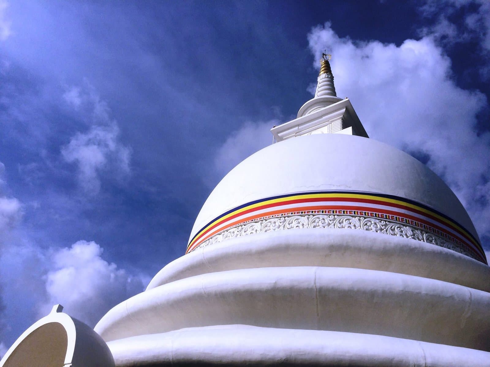 A white Buddhist stupa with a golden spire, viewed from below against a blue sky